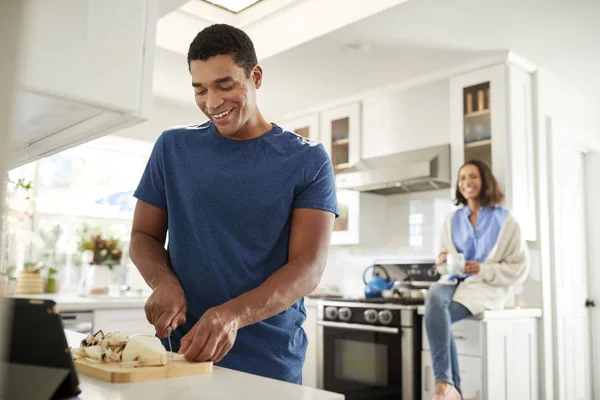 年轻的成年人站在厨房里准备食物 他的伴侣坐在他身后的厨房工作台上 专注于前景 — 图库照片