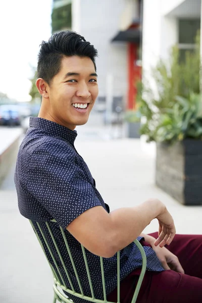 街の通りの椅子に座るミレニアル世代のアジア人男性 カメラに向かって笑顔 クローズアップ — ストック写真