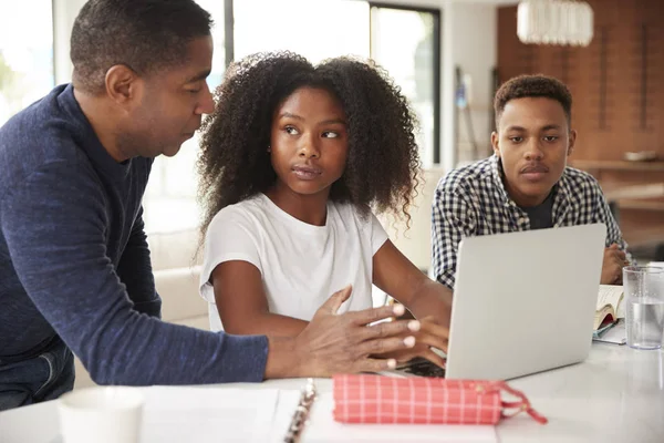 ラップトップコンピュータを使用して宿題をする彼の十代の子供たちを助ける中年の黒人男性 — ストック写真