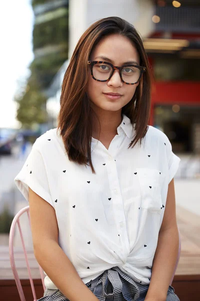 时髦的年轻亚洲女人戴着眼镜坐在椅子上在街上看着相机 — 图库照片