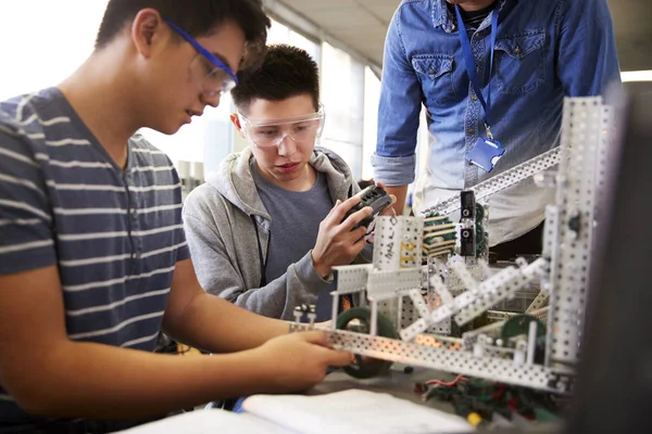 理科ロボティクスや工学の授業で機械を作る2人の男子大学生を持つ教師 — ストック写真
