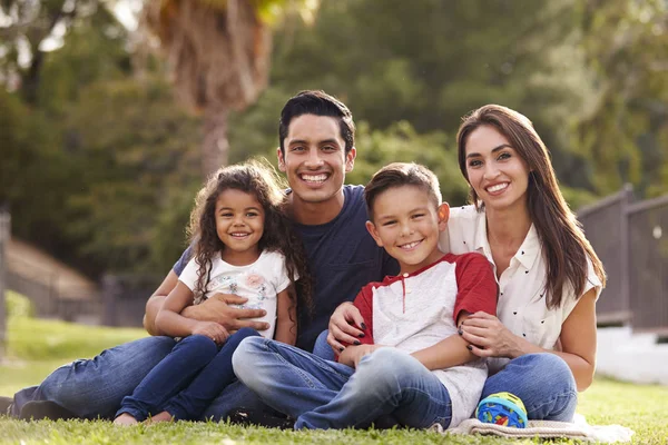 Feliz Joven Familia Hispana Sentada Hierba Parque Sonriendo Cámara — Foto de Stock