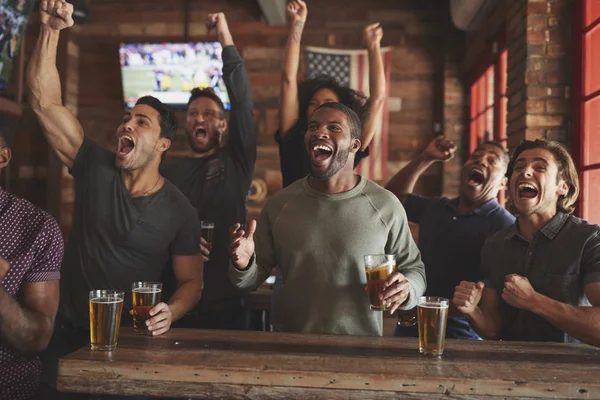スポーツバーで画面上のゲームを見ながら祝う男性の友人のグループ — ストック写真