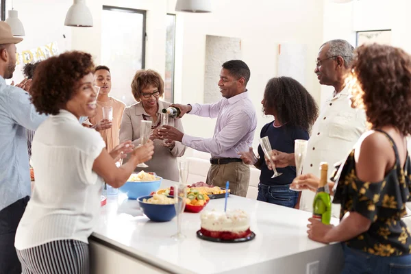 中年の黒人男性が3世代家族と一緒に自宅で祝うためにシャンパンを注ぐ — ストック写真
