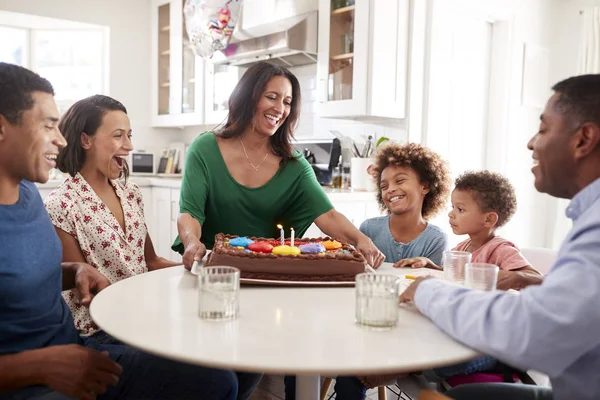 誕生日を祝う台所で一緒に座って興奮した3世代の家族 おばあちゃんがテーブルにケーキを持って来る — ストック写真