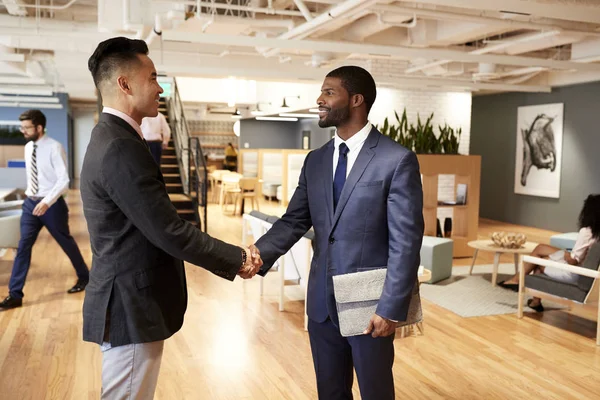 Two Businessmen Meeting And Shaking Hands In Modern Open Plan Office