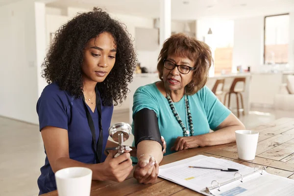 在宅訪問中の女性医療従事者が高齢者の血圧をチェック — ストック写真