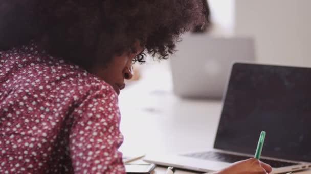 ミレニアル世代の黒人ビジネスウーマンがオフィスのテーブルに座ってメモを作り クローズアップ — ストック動画