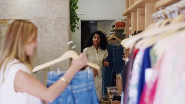 ファッションストアでジーンズを選択する女性の顧客を支援するセールスアシスタント スローモーションで撮影 — ストック動画