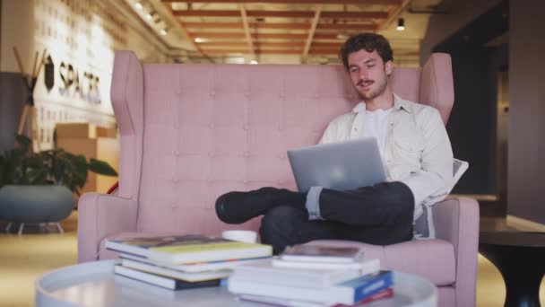ラップトップコンピュータを使用してオフィスロビーのソファに座ってミレニアル白人男性クリエイティブ — ストック動画