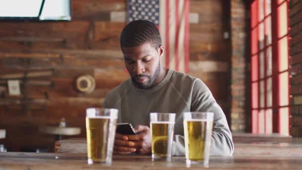 Joven Sentado Bar Deportivo Mirando Teléfono Móvil Bebiendo Cerveza Filmado — Vídeos de Stock