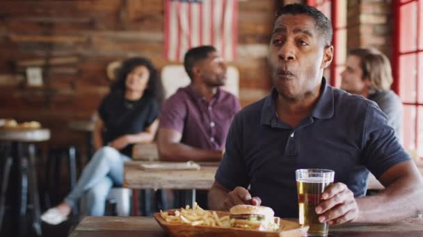 Mature Man Sitting Sports Bar Watching Game Whilst Eating Burger — Stock Video
