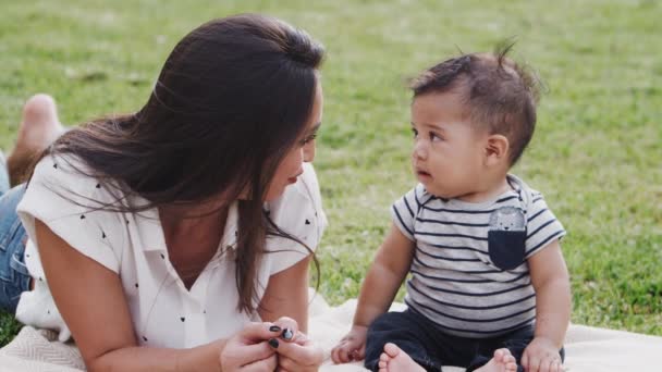 ミレニアル世代のヒスパニック系の母親は 彼女の赤ちゃんの男の子と話して公園の草の上に横たわって クローズアップ — ストック動画