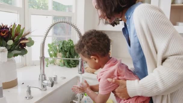 千禧年妈妈站在厨房水槽帮助她的儿子洗手 侧视图 — 图库视频影像
