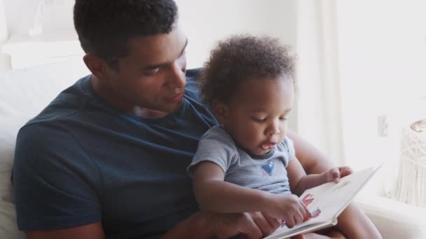 ミレニアル世代のアフリカ系アメリカ人の父親が幼児の息子と一緒に本を読んでいるのを見て クローズアップ — ストック動画