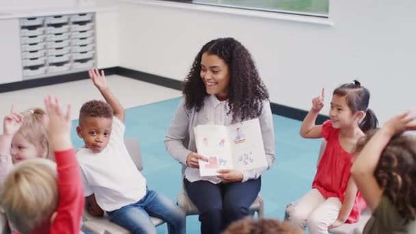 教室で子供たちに本を見せ 話すために手を挙げる若い女子幼児学校の教師 — ストック動画