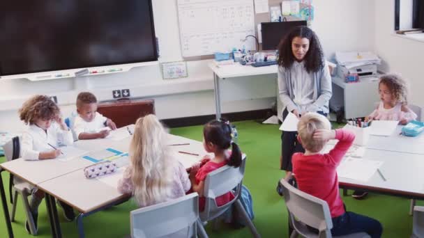 微笑的女幼儿学校老师坐在教室前与学校的孩子交谈 — 图库视频影像