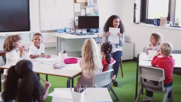 教室で学校の子供たちにワークシートを見せる女子幼児学校の教師 — ストック動画