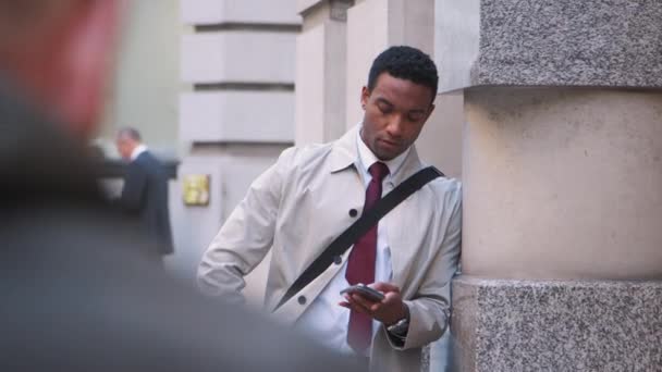 年轻的黑人商人靠在伦敦街头的墙上用他的智能手机 选择性的焦点 腰部向上 — 图库视频影像
