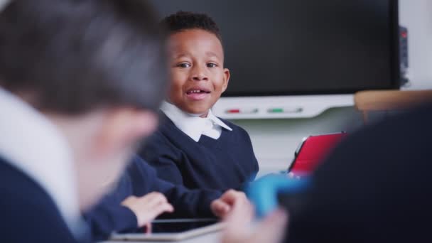 小学校の授業でクラスメートと話すテーブルに座っている黒人の男子生徒 選択的な焦点 — ストック動画