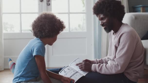 中年黑人父亲坐在地板上在家里帮助他的前十几岁的儿子与玩具建设工具包的说明 低角度 侧视图 — 图库视频影像
