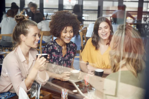 Cuatro jóvenes amigas se reúnen en la mesa en la cafetería y — Foto de Stock