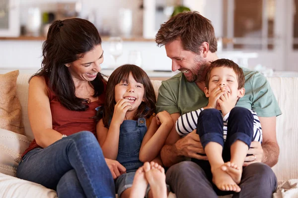 中等成年白人夫妇和他们的两个年幼的孩子坐在家里的一张小瓦上互相微笑 — 图库照片