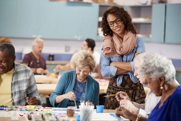 Group Of Retired Seniors Attending Art Class In Community Centre With Teacher