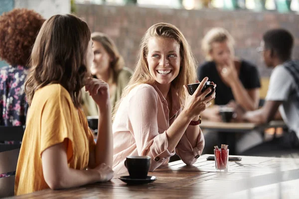 Dos amigas sentadas en la mesa en la cafetería y hablando — Foto de Stock