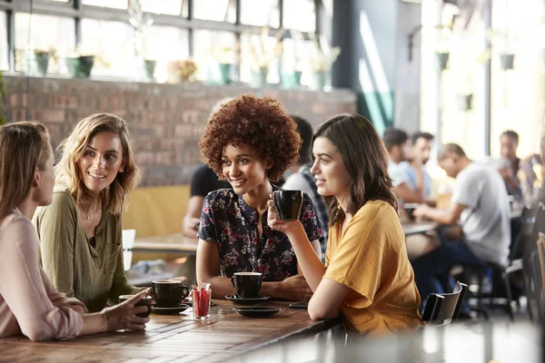 四个年轻的女性朋友会议坐在餐桌上的咖啡店和谈话 — 图库照片