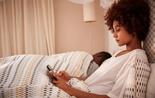 ミレニアル世代のアフリカ系アメリカ人女性がスマートフォンを使ってベッドに座り サイドビュー クローズアップ — ストック写真