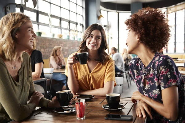 三个年轻的女性朋友会议坐在餐桌上的咖啡店和谈话 — 图库照片