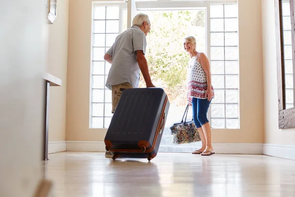 休暇に出発しようとしているスーツケースを持って玄関のそばに立つシニアカップル — ストック写真