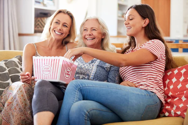 大人の娘と十代の孫娘が自宅のソファで映画を見てポップコーンを食べる母親 — ストック写真