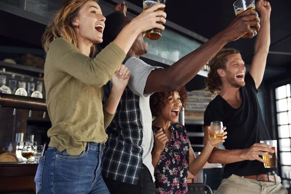 一组男性和女性的朋友庆祝 而观看游戏在屏幕上在体育酒吧 — 图库照片