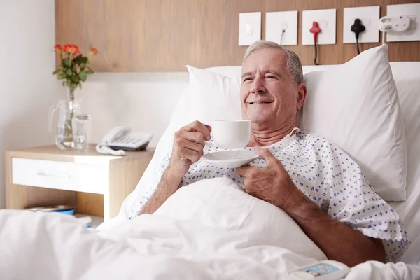 Male Senior Patient Lying Hospital Bed Enjoying Hot Drink — Stock Photo, Image
