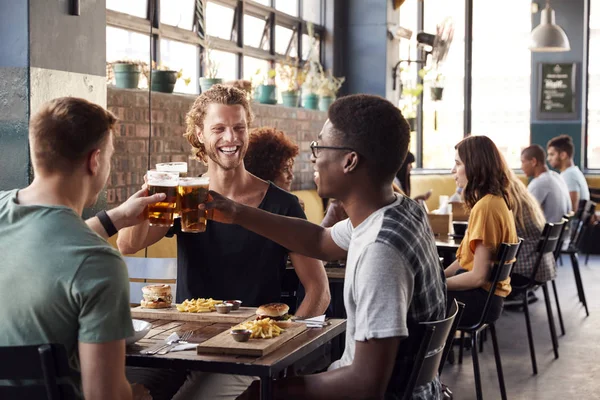 Trois jeunes amis masculins réunion pour les boissons et la nourriture faisant un à — Photo