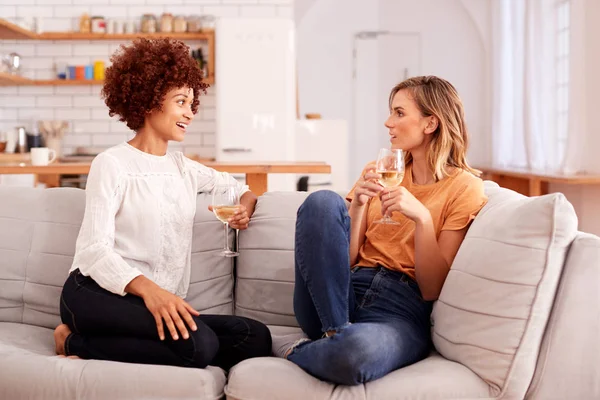 ワインのグラスを持って自宅でソファでくつろぐ2人の女性の友人が一緒に話す — ストック写真