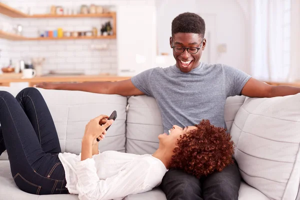 年轻夫妇放松在沙发在家里看手机在一起 — 图库照片