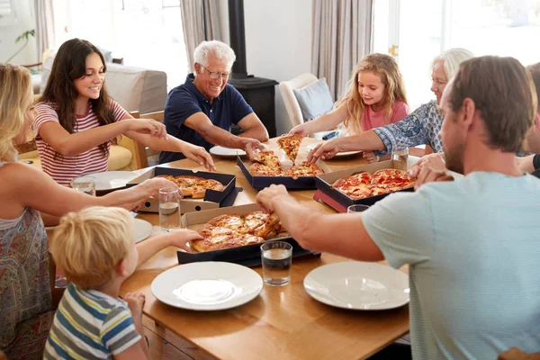 テーブルの周りに座ってテイクアウトピザを一緒に食べる多世代の家族 — ストック写真