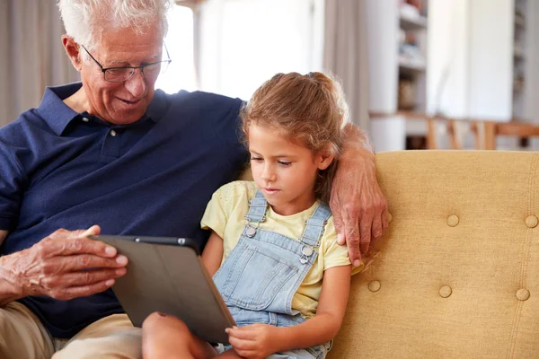 祖父坐在与孙女坐在Sofa使用数字平板电脑在家里 — 图库照片
