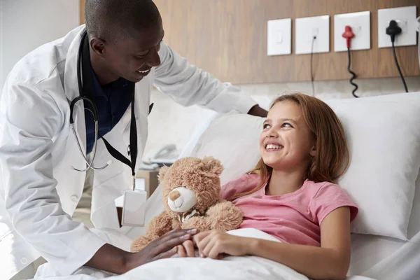 病院のベッドに横たわっている女の子を訪問する男性医師はテディベアを抱きしめる — ストック写真