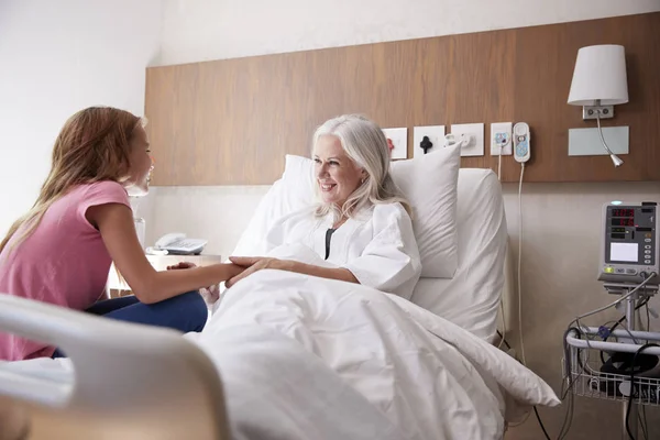 病院のベッドで祖母と面会し 話す孫娘 — ストック写真
