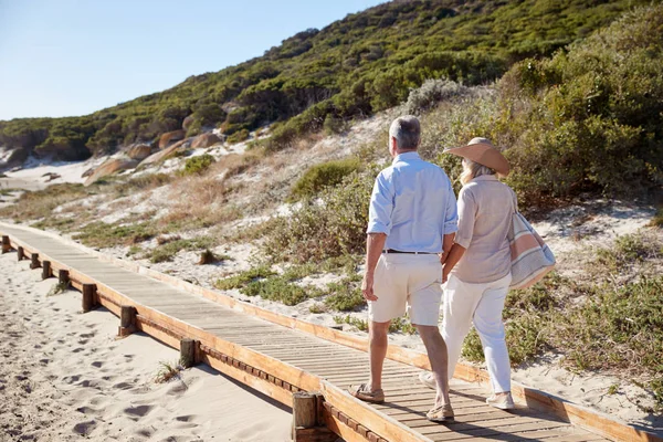 老年白人夫妇沿着木制长廊走在沙滩上手牵手 后视图 — 图库照片
