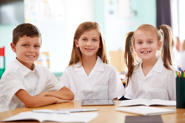 三名小学生在书桌上使用数字平板电脑穿着制服的肖像 — 图库照片