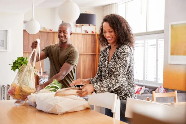 Couple Returning Home From Shopping Trip Unpacking Plastic Free Grocery Bags