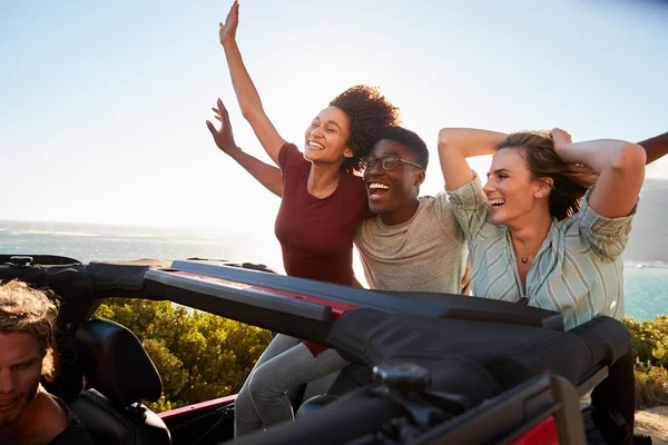 兴奋的千禧一代朋友在一辆开着的汽车后面旅行 手臂在空中 — 图库照片