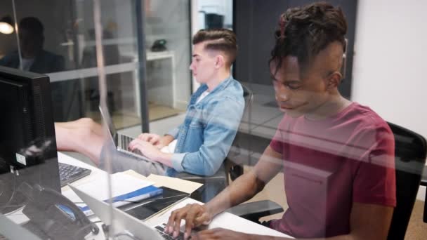 ガラスのオフィスの小部屋に座ってコンピュータで働く2人の若い男性の高い眺め 閉じる ガラスを通して見える — ストック動画