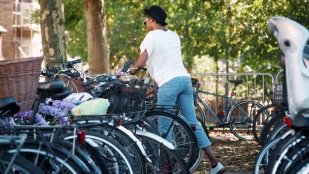 티셔츠 청바지 선글라스를 착용한 여성이 자전거를 주차하고 크로스바디 핸드백을 착용하고 — 비디오