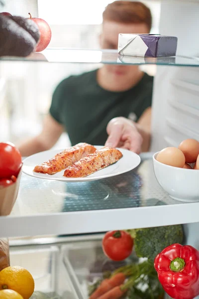 年轻人伸手在冰箱里吃健康食品 在盘子里吃新鲜的鲑鱼 — 图库照片